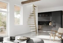 Engineering compact staircases for urban construction Bright open-plan living area with a floating wooden staircase, black contemporary kitchen, and large windows letting in light.