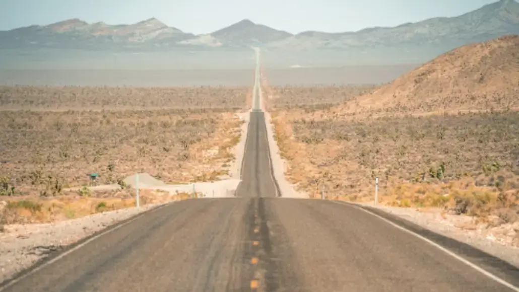 Long straight road stretches through a desert toward distant mountains under a clear sky.