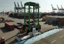 KoneCranes straddle carrier outfitted with zepp.solutions hydrogen system Green gantry crane at a port terminal with stacked shipping containers and a marked 'HYDROGEN ZONE' lane nearby.